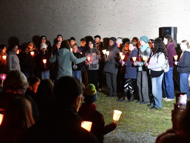 Der Chor des Ohm Gymnasium singt bei Ankunft im Fackelzug am Ort des Massakers in Cumiana. Alle Sänger*innen und das Publikum haben Fackeln in der Hand. 