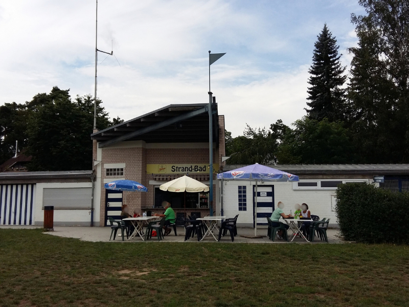 Ein Kiosk mit bestuhlter Außenfläche und Menschen.