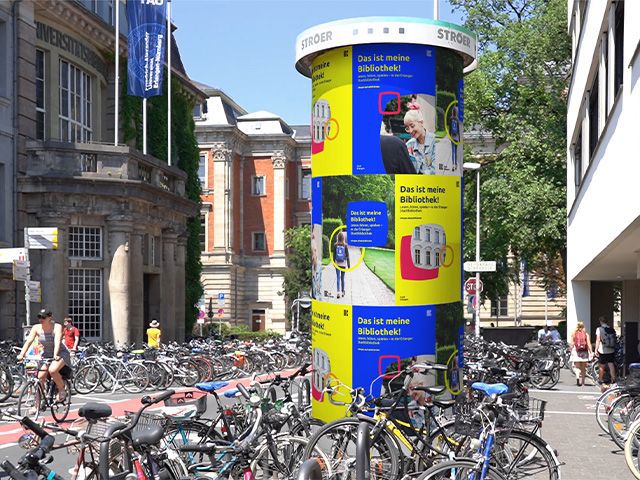 Litfasssäule in der Innenstadt, um ihr herum stehen viele Fahrräder 