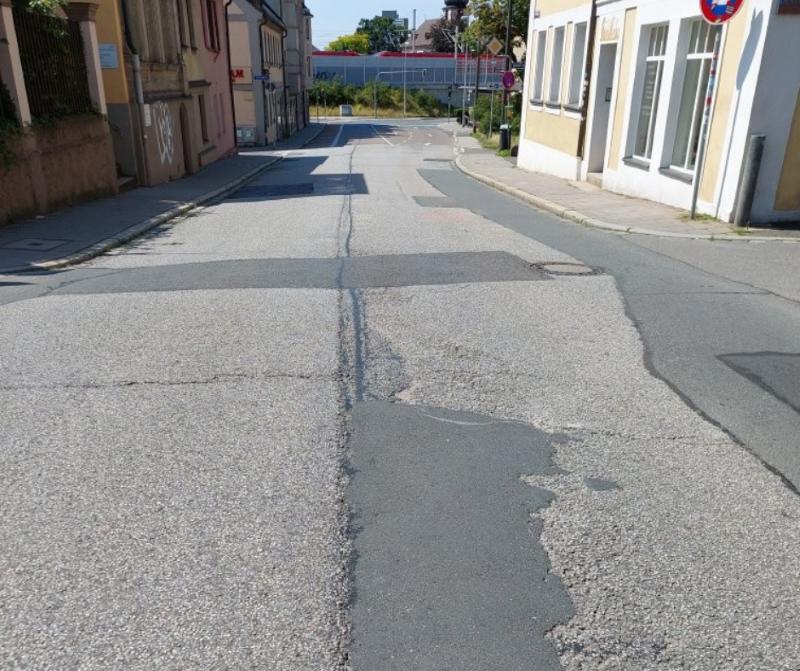 Eine sanierungsbedürftige Straße mit Häuser links und rechts. 