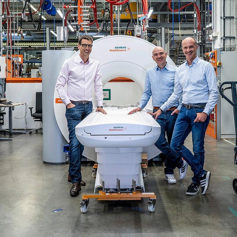 Drei Männer in einer Werkhalle an einer Maschine.