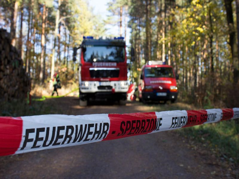 Zwei Feuerwehrfahrzeuge auf einem Waldweg, davor ein Absperrband der Feuerwehr.