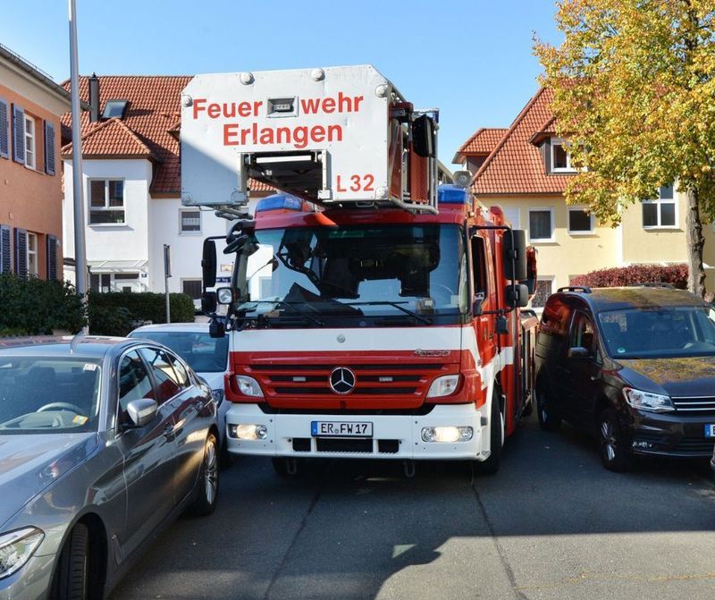 Ein Feuerwehrfahrzeug fährt durch eine von Autos am Straßenrand zugeparkte Straße.