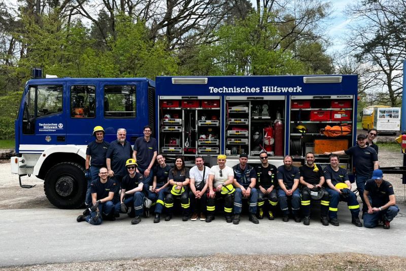 Vor einem Einsatzfahrzeug des Technischen Hilfswerks (THW) sitzt und steht eine Gruppe von Einsatzkräften in Uniform zu einem Gruppenfoto.