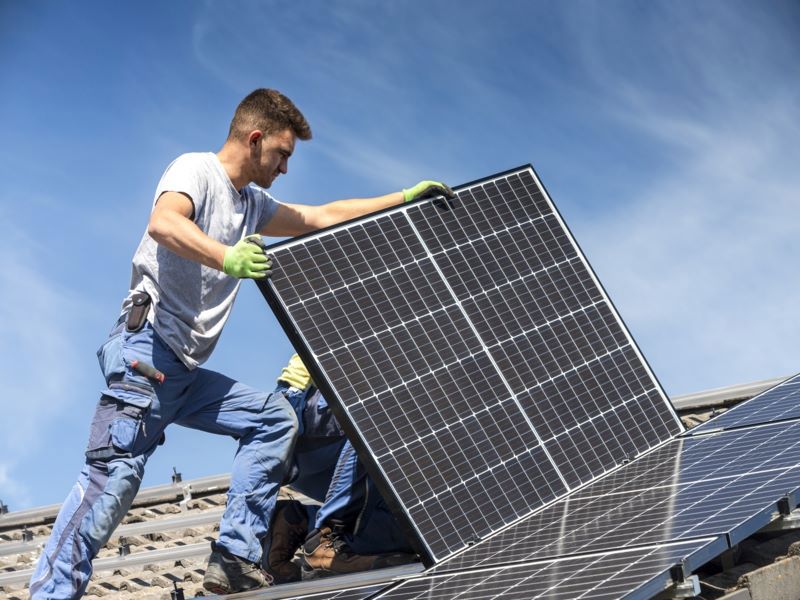 Ein Mann mit Photovoltaigplatten auf einem Dach.