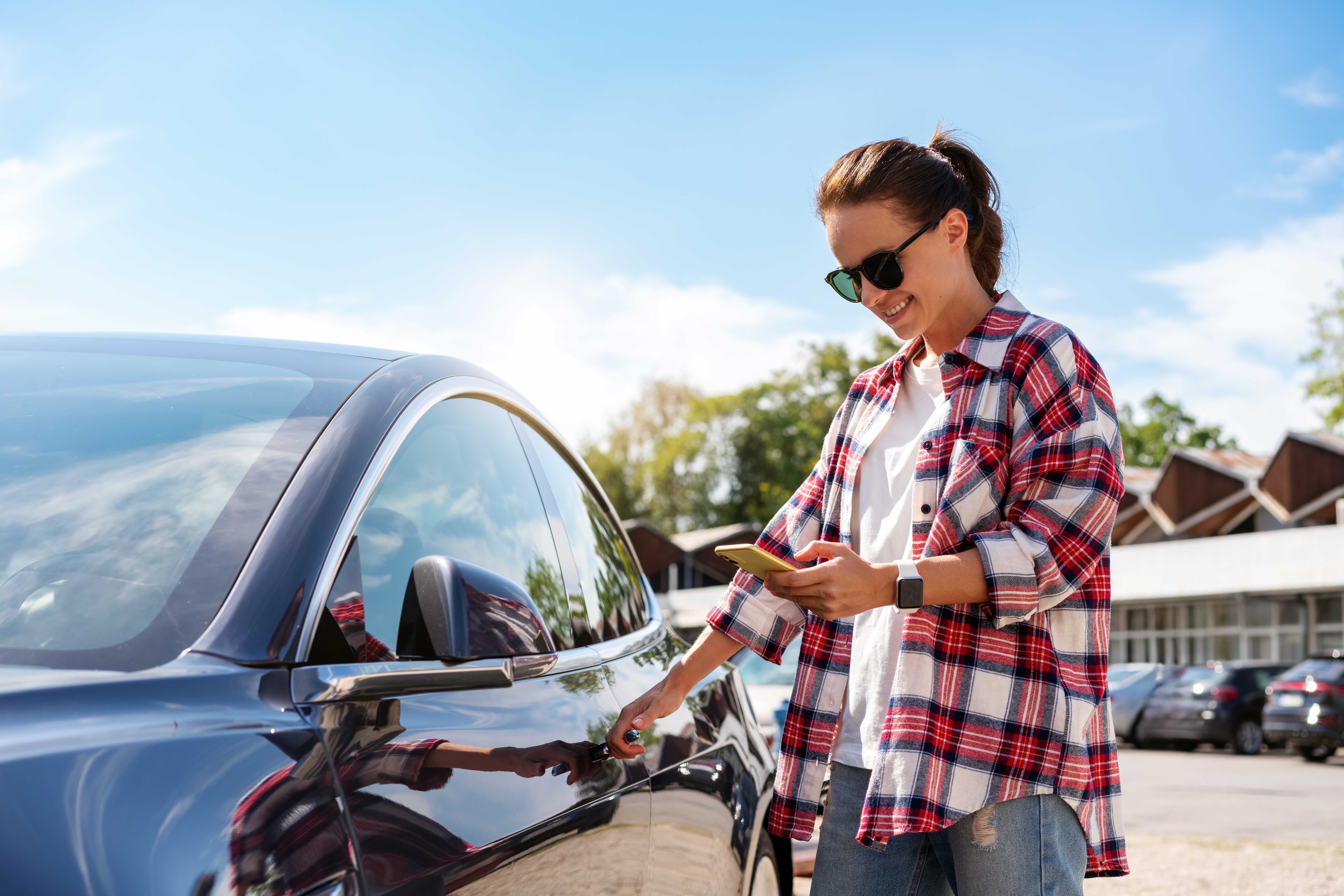 Eine Frau in legerer Kleidung entriegelt ein Carsharing Fahrzeug mithilfe ihres Smartphones und einer mobilen App.