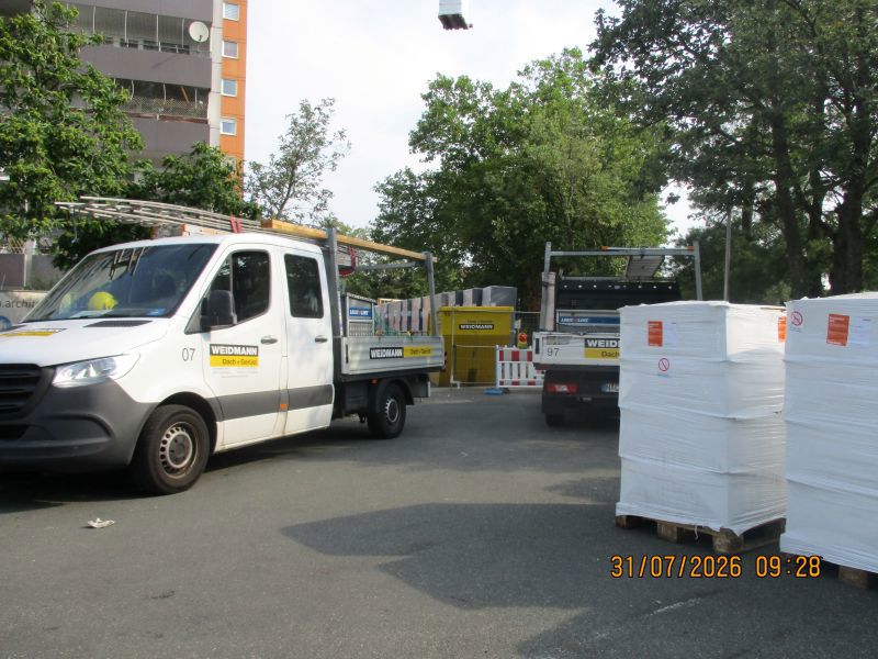 Transporter stehen an einer Baustelle, im Hintergrund ist ein Haus.