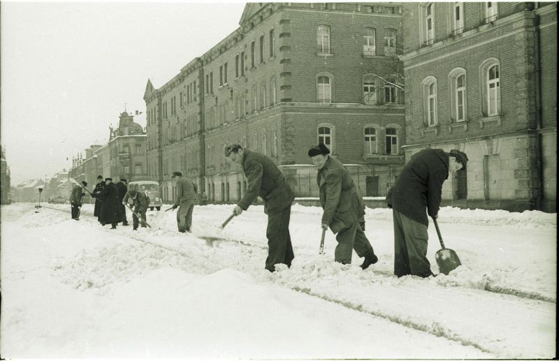 Eine verschneite Straße wird von mehreren Männern geräumt. 