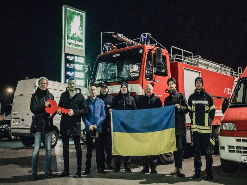 Ein rotes Feuerwehrfahrzeug, vor dem Menschen mit einer ukrainischen Flagge stehen.