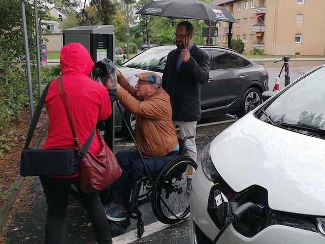 Ein Mann im Rollstuhl betankt sein Auto. 