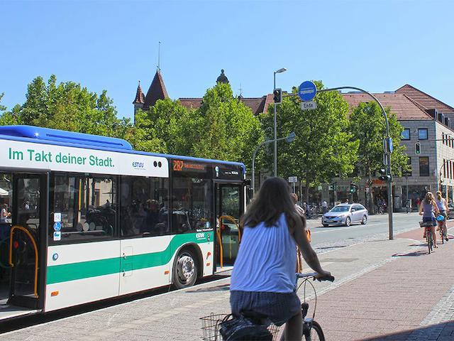 Bushaltestelle Henkestraße mit Bus, Radfahrerin und Passanten.