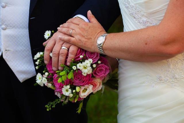 Ein Ehepaar mit einem Blumenstrauß halten die Hände.