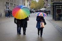 A couple with an umbrella in a rainbow design and other people.