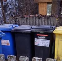 Blue, black and yellow garbage cans on a garden fence.