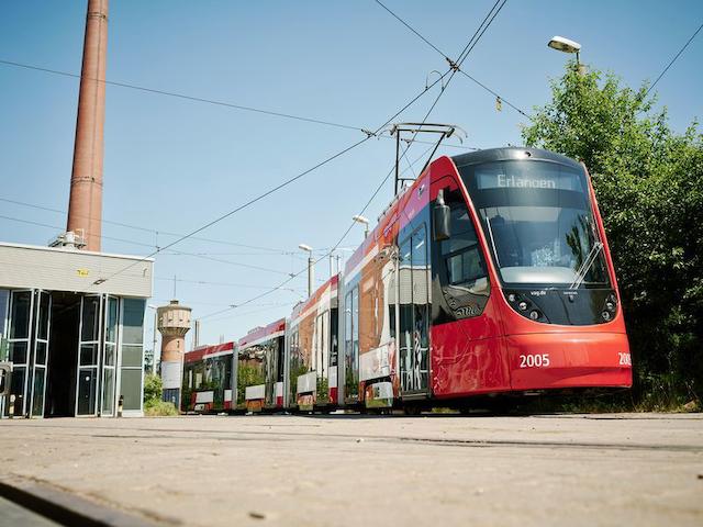 Eine rote Straßenbahn rechts neben einem Gebäude. 
