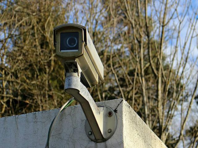 A video camera fixed to a wall, trees in the background.