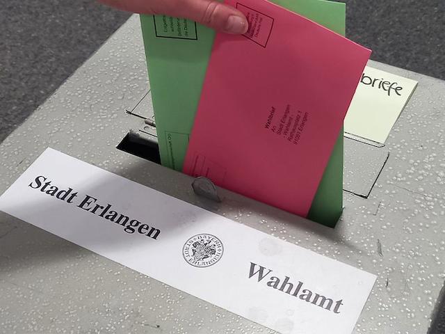 A red and green ballot paper are thrown into a gray ballot box.