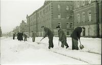 Eine verschneite Straße wird von mehreren Männern geräumt. 