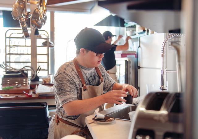 Young man with a disability works in the kitchen of a restaurant