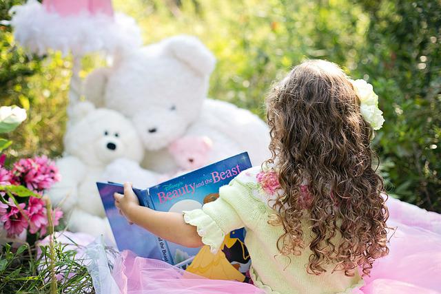 Ein sitzendes Kind hält ein Buch in der Hand, vor ihm sitzen zwei Teddybären.