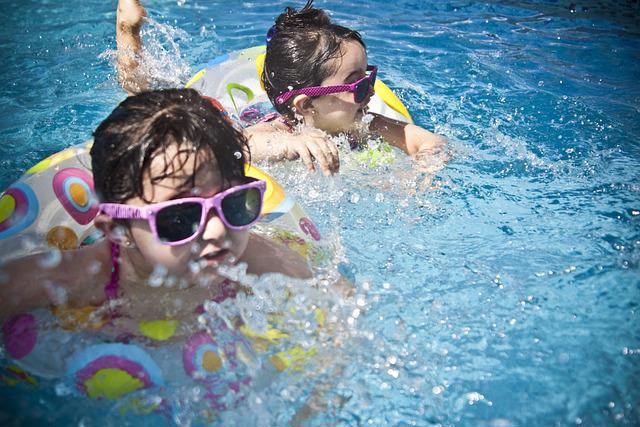 Yüzme havuzunda güneş gözlüklü iki çocuk.