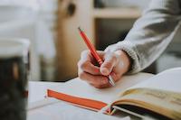 Hand holds a pen and writes something down in a book.