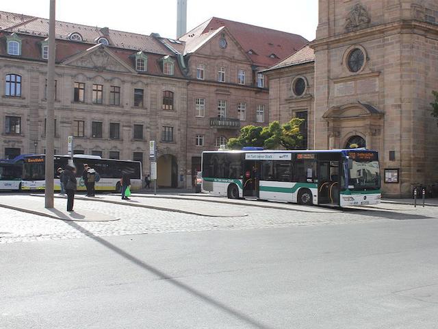 Bushaltestelle Hugenottenplatz mit zwei Bussen und Passanten
