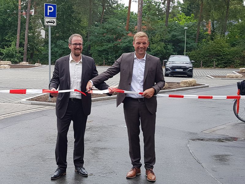 Oberbürgermeister Florian Janik und Sportbürgermeister Jörg Volleth durchschneiden ein rot weißes Band auf dem Parkplatz.