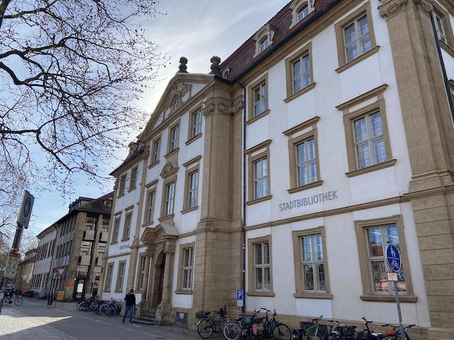 Palais Stutterheim mit Eingang Stadtbibliothek, vor dem Gebäude läuf ein Mann, dazu mehrere abgestellte Fahrräder