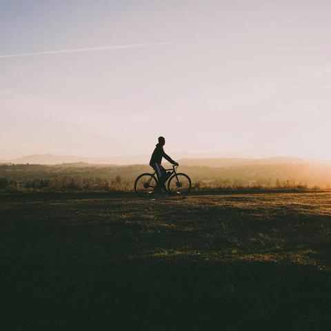 Ein einzelner Radfahrer fährt durch Felder im Sonnenuntergang.