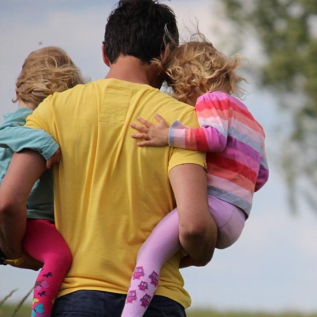 Father carries twins through field.