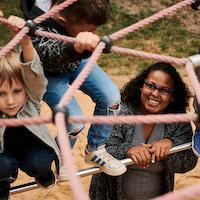 Kinder spielen mit Betreuerin auf Spielplatz.