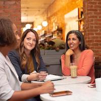 Frauen sitzen an Tisch und unterhalten sich.