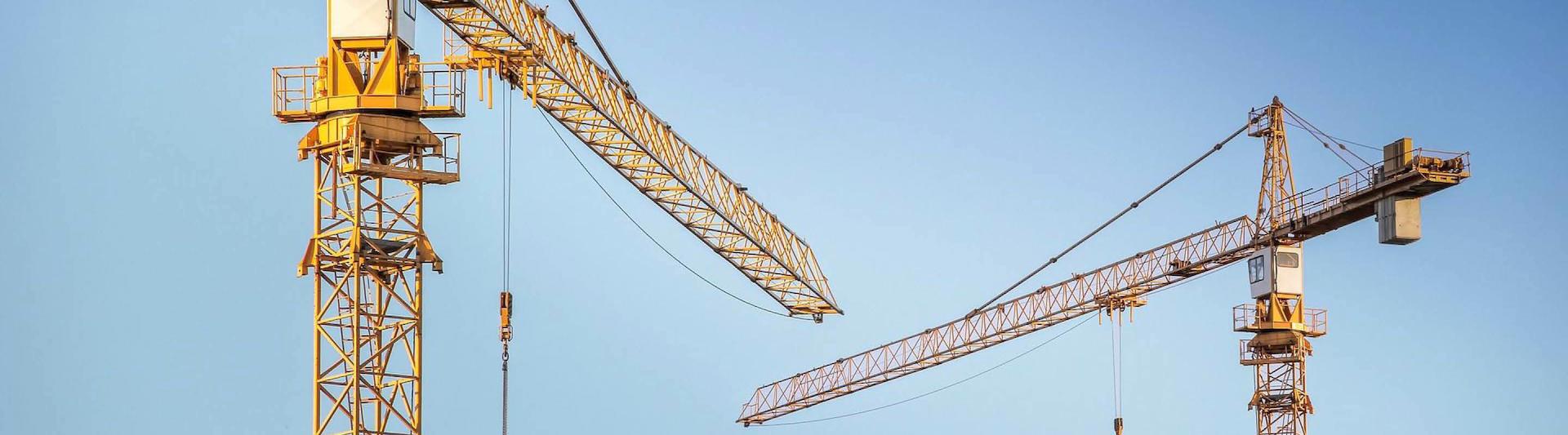 Two construction site cranes against blue sky.